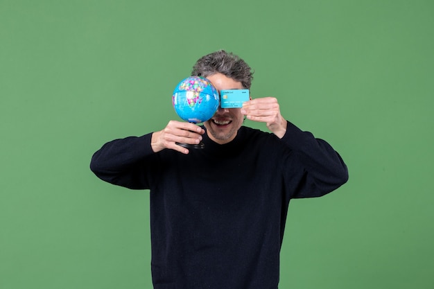 Portrait de jeune homme tenant un globe terrestre et une carte de crédit fond vert argent nature professeur banque