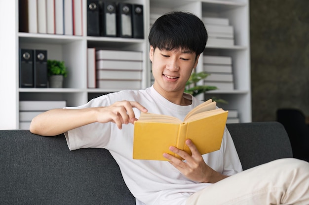 Portrait d'un jeune homme tenant un livre en papier ou un journal assis sur le canapé à la maison dans le salon en train de lire de la littérature ou de vérifier son programme de travail