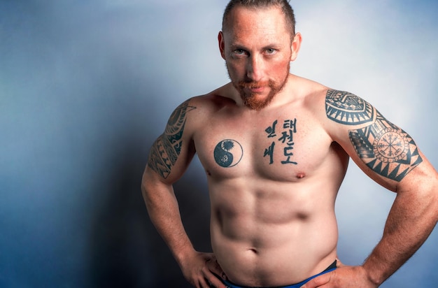 Portrait d'un jeune homme torse nu en forme avec des tatouages isolé sur blanc