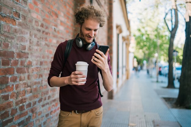 Portrait de jeune homme utilisant son téléphone portable en marchant à l'extérieur dans la rue. Communication et concept urbain.