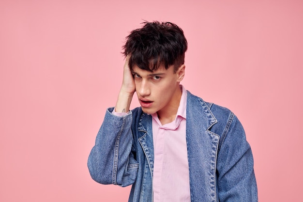 Portrait d'un jeune homme en veste en jean de vêtements élégants pour jeunes posant sur fond rose inchangé