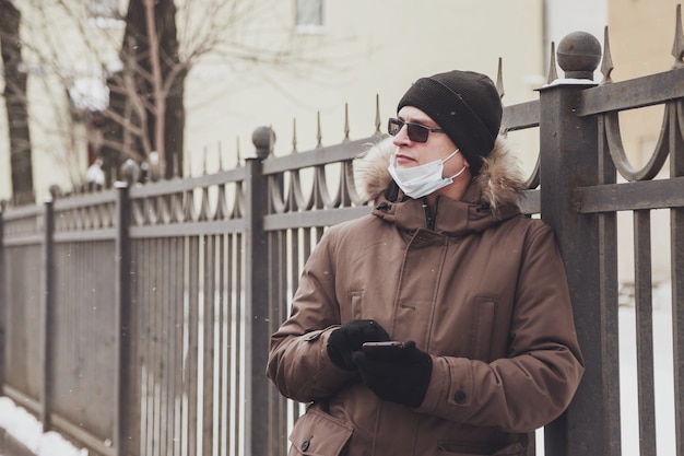 Portrait de jeune homme en vêtements d'hiver décontractés avec lunettes et masque médical sur la ville de marche