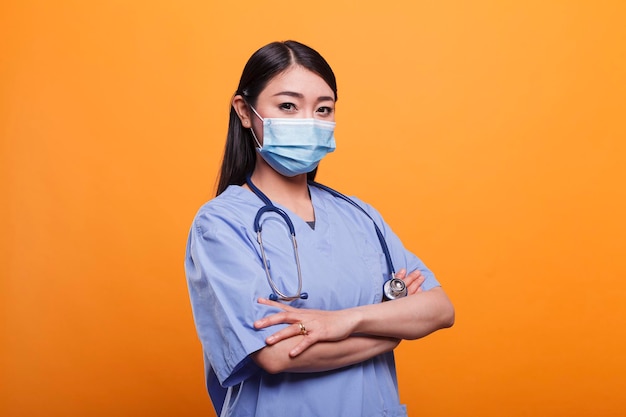 Portrait d'une jeune infirmière asiatique d'une clinique de soins de santé pour adultes portant un stéthoscope et un masque protecteur. Soignant hospitalier portant un instrument médical, un uniforme bleu et un masque de protection contre les virus.