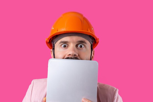 Portrait d'un jeune ingénieur en construction portant un casque orange dans une veste rose debout sur fond de studio rouge Un homme avec une tablette dans ses mains