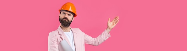 Portrait d'un jeune ingénieur en construction portant un casque orange dans une veste rose debout sur fond de studio rouge Un homme avec une tablette dans ses mains