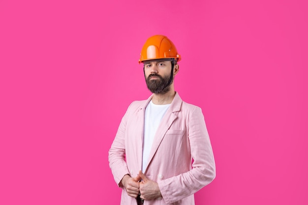 Portrait d'un jeune ingénieur en construction portant un casque orange dans une veste rose debout sur fond de studio rouge