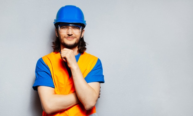 Portrait d'un jeune ingénieur ouvrier confiant portant des équipements de sécurité; casque bleu, lunettes transparentes