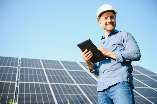 Le portrait d'un jeune ingénieur vérifie avec le fonctionnement de la tablette avec la propreté du soleil sur le champ des panneaux solaires photovoltaïques Concept technologie des énergies renouvelables service d'électricité énergie verte