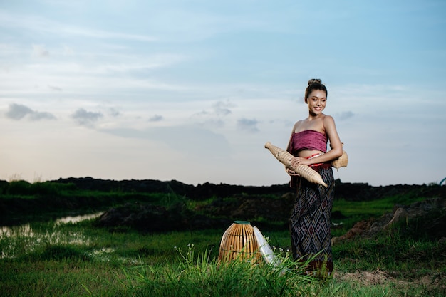 Portrait Jeune Jolie Femme Asiatique Dans De Beaux Vêtements Traditionnels Thaïlandais Dans Une Rizière, Elle Se Tient Debout Et Tient Du Matériel De Pêche