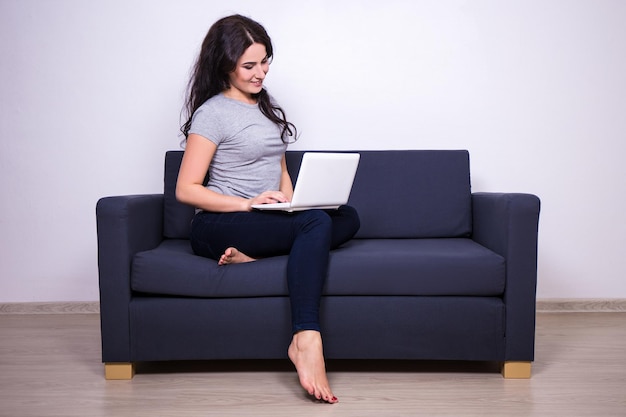 Portrait de jeune jolie femme assise sur un canapé et utilisant un ordinateur à la maison