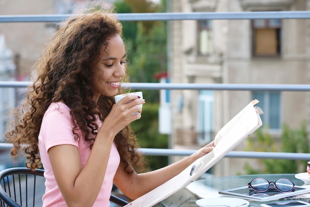 Photo portrait de jeune jolie femme lisant le journal sur la terrasse d'été de la ville
