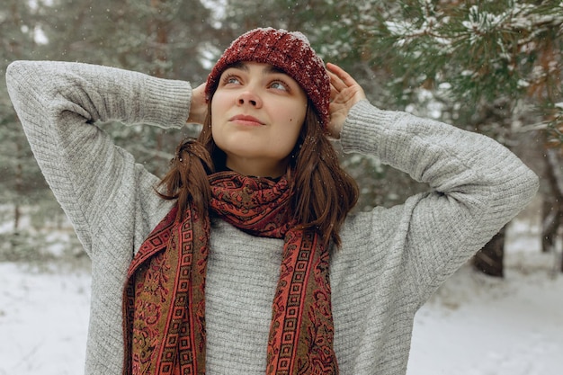 Portrait de jeune jolie femme en pull chaud et écharpe profitant du temps neigeux dans la forêt d'hiver
