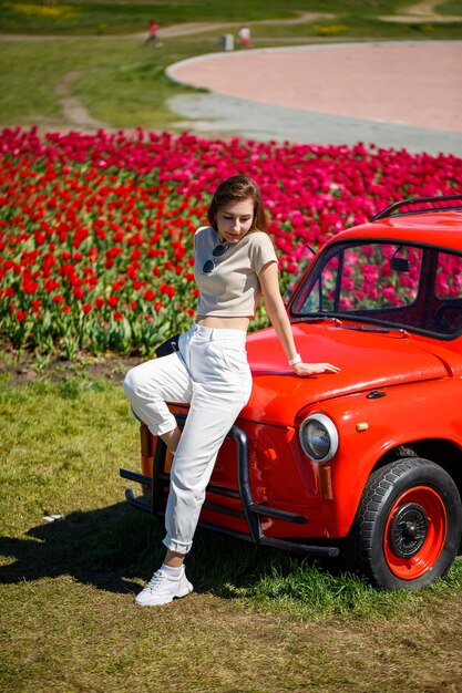 Portrait de jeune jolie femme se penchant sur une voiture cabriolet rustique dans des champs de tulipes colorées Chilliwack Tulip Ftstival British Columbia Canada