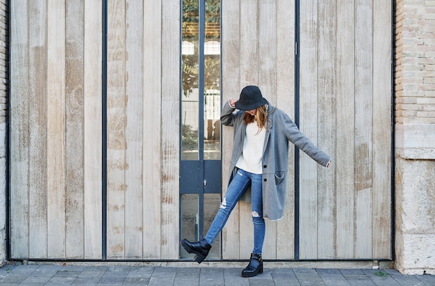 Un portrait jeune jolie fille de race blanche, vêtue d'une veste grise, un pull blanc et un chapeau.