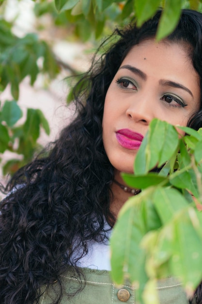 Portrait d'une jeune Latina aux cheveux bouclés dans le parc. Femme hispanique debout à l'extérieur et regardant sur le côté.