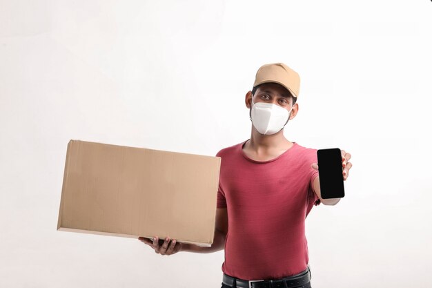 Portrait d'un jeune livreur heureux excité en casquette debout sur fond blanc. Regarder la caméra montrant l'affichage du téléphone mobile.