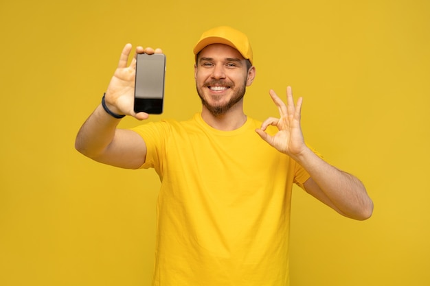 Portrait d'un jeune livreur heureux excité en casquette jaune debout isolé sur mur blanc