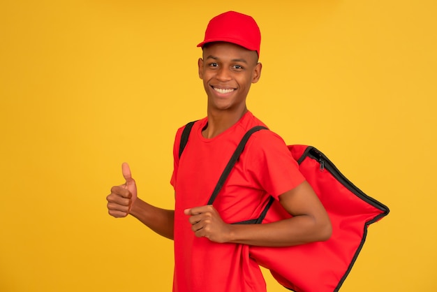 Portrait d'un jeune livreur regardant la caméra et montrant le pouce vers le haut en se tenant debout sur un fond jaune isolé. Concept de service de livraison.