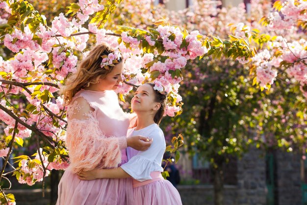 Portrait d'une jeune maman avec sa fille debout sous un sakura Belle maman et sa fille portant les mêmes vêtements