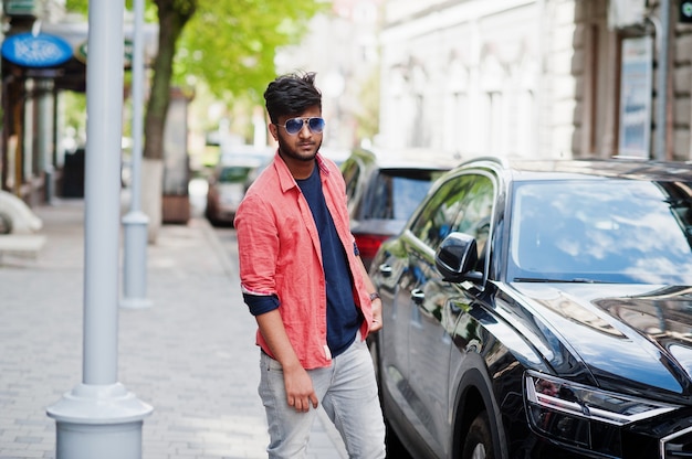 Portrait de jeune mannequin indien élégant pose dans la rue à lunettes de soleil contre la voiture.