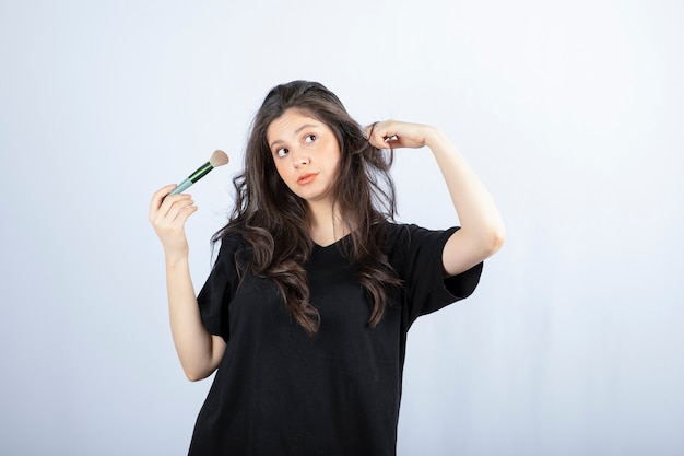 Portrait de jeune mannequin avec maquillage avec pinceau debout sur un mur blanc.