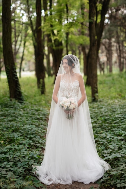 Portrait d'une jeune mariée élégante sur un chemin dans une forêt de feuillus avec un bouquet