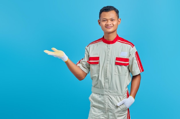 Portrait de jeune mécanicien asiatique souriant montrant l'espace de copie dans les paumes sur fond bleu