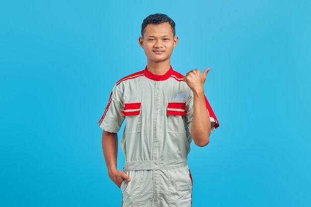Portrait de jeune mécanicien heureux pointant le doigt sur l'espace de copie sur fond bleu