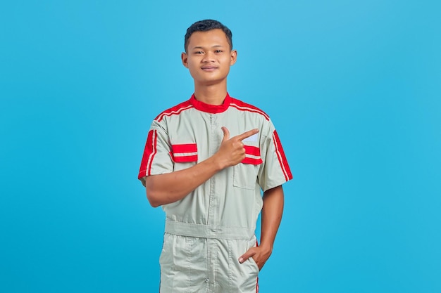 Portrait de jeune mécanicien souriant pointant le doigt sur l'espace de copie sur fond bleu