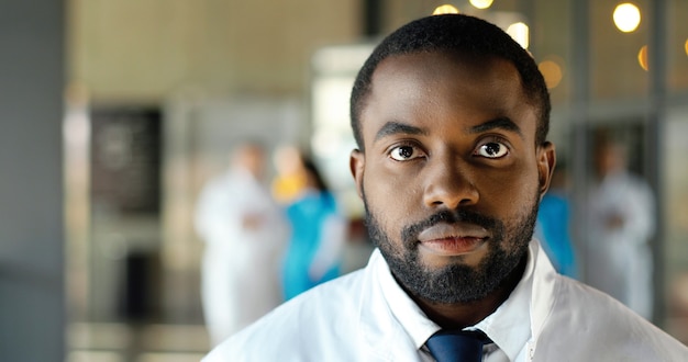 Portrait de jeune médecin afro-américain regardant la caméra et souriant joyeusement. Beau sourire de médecin de sexe masculin heureux. Medic en robe blanche en clinique. Intérieur.