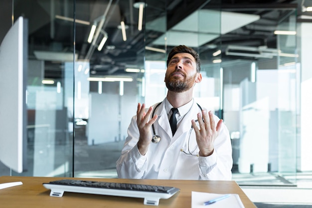 Portrait d'un jeune médecin barbu priant Dieu pour le succès avec espoir levant les mains vers le ciel l'homme l'homme demande bonne chance et prie pour une solution réussie à la question de l'aide