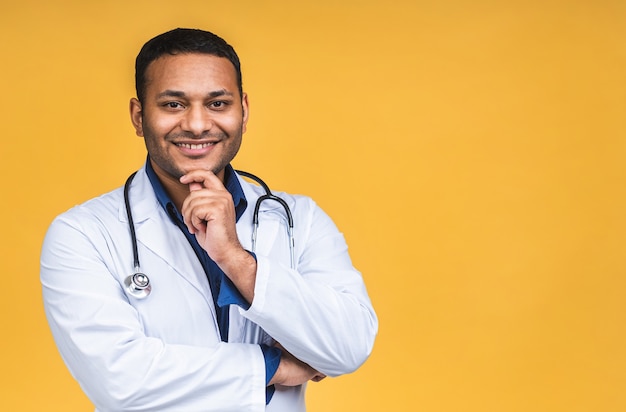 Portrait de jeune médecin noir indien afro-américain avec stéthoscope sur le cou en blouse médicale debout isolé sur fond jaune.