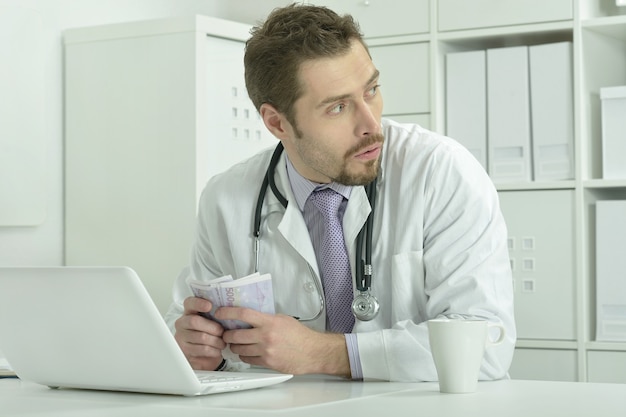 Portrait de jeune médecin avec ordinateur portable et argent