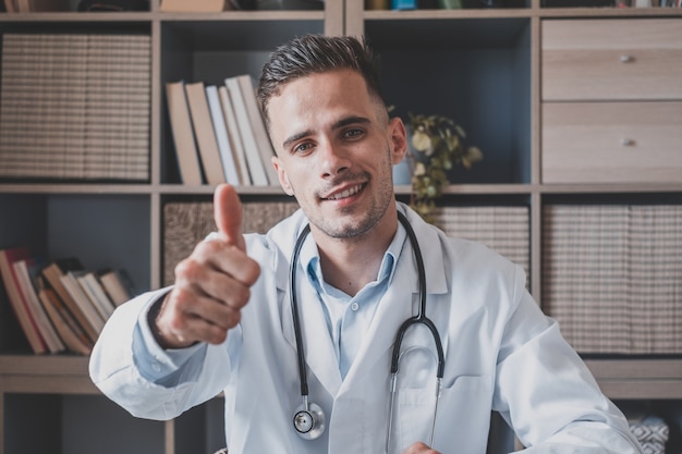 Portrait d'un jeune médecin de race blanche heureux montre le pouce vers le haut, donne une recommandation à la clinique. Un homme souriant, un médecin généraliste ou un thérapeute recommande un service de bonne qualité dans un hôpital privé. Notion de médecine.