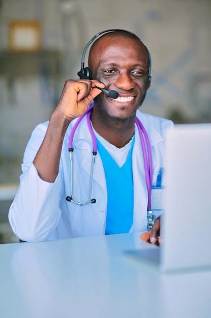 Portrait d'un jeune médecin de sexe masculin portant un casque lors de l'utilisation d'un ordinateur au bureau dans une clinique