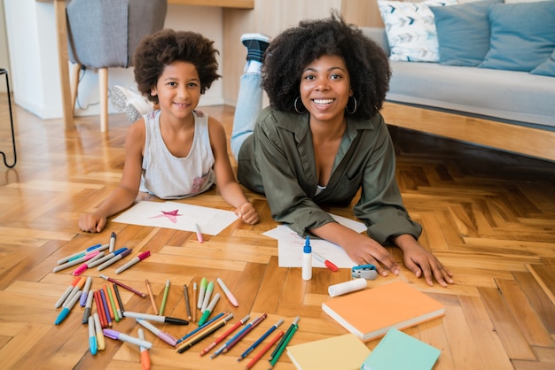 Portrait de jeune mère et fils dessin avec des crayons de couleur sur un sol chaud à la maison