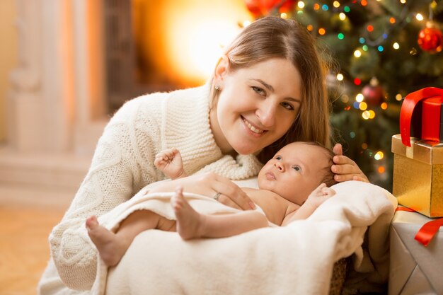 Portrait d'une jeune mère heureuse posant avec un nouveau-né à la maison décorée pour Noël