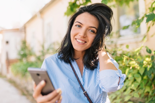 Portrait de jeune modèle féminin positif dans des vêtements élégants partage des fichiers multimédias sur les réseaux sociaux en étant heureux de se détendre dans la ville Concept de mode de vie et de technologie des gens