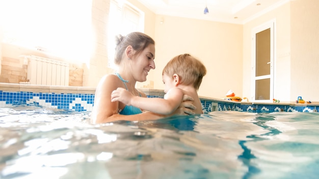 Portrait d'un jeune mothet joyeux et joyeux avec un petit garçon de 3 ans jouant dans la piscine de la maison. Enfant apprenant à nager avec un parent. Famille s'amusant en été