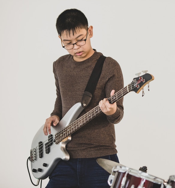 Portrait d'un jeune musicien adolescent jouant de la guitare basse en studio. Étudiant junior professionnel jouant d'un instrument avec un fond blanc. Jeune adolescent bassiste pratiquant pour le spectacle