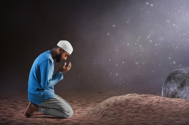 Photo portrait d'un jeune musulman asiatique pleurant de tristesse avec une barbe priant sur un cimetière