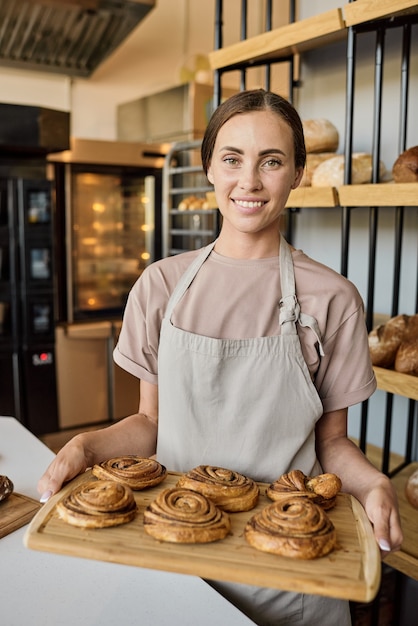 Portrait d'une jeune pâtissière heureuse debout près du lieu de travail et vendant de la pâtisserie fraîche