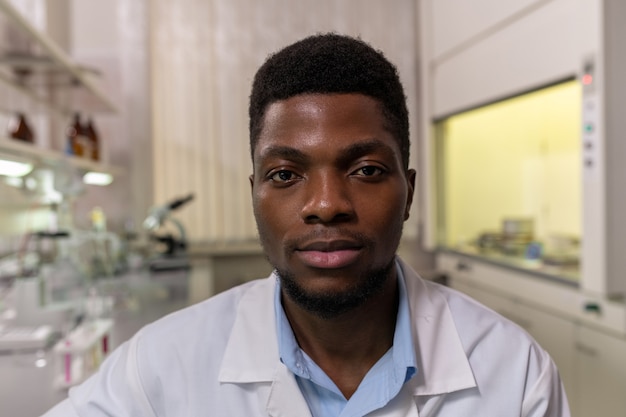 Portrait de jeune scientifique africain regardant la caméra tout en travaillant dans le laboratoire