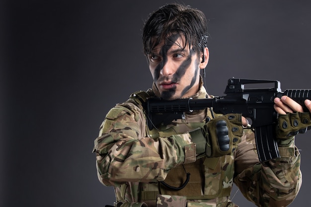 Portrait de jeune soldat en camouflage visant une mitrailleuse sur un mur sombre