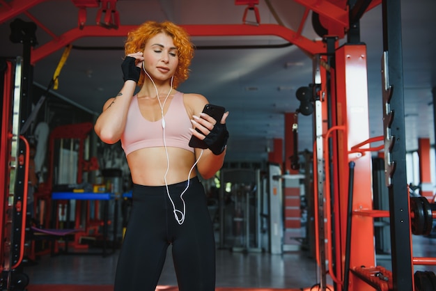 Portrait de jeune sportive avec smartphone, écouter de la musique dans une salle de sport