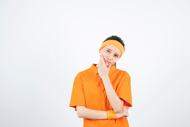 Portrait de jeune sportive en tenue orange pensant sur blanc.