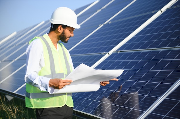 Portrait d'un jeune technicien indien portant un casque blanc debout près de panneaux solaires contre le ciel bleuOuvrier industriel installation de système solaire concept de génération d'énergie verte renouvelable