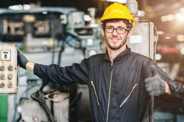 Portrait de jeune travailleur américain heureux profiter de sourire heureux de travailler dans une usine industrielle lourde.Tumb avec contrôleur de machine.