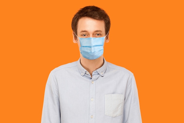 Portrait d'un jeune travailleur avec un masque médical chirurgical debout et regardant la caméra en souriant. concept de soins de santé et de médecine. tourné en studio intérieur isolé sur fond orange.