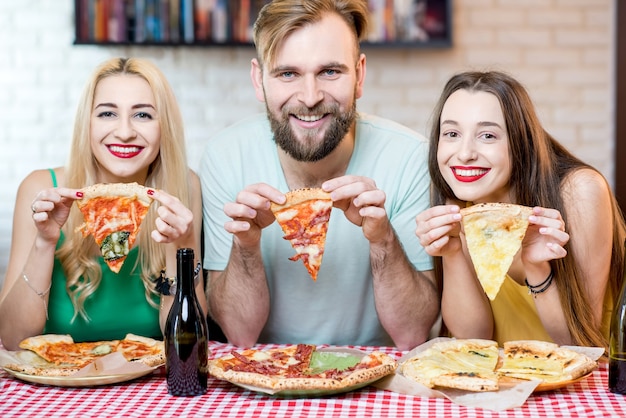 Portrait De Jeunes Amis Drôles Vêtus Avec Désinvolture De T-shirts Colorés Tenant Une Tranche De Pizza à La Maison